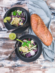 Top view italian ciabatta and fresh vegetable salad in a dark bowl. Salad with radish, red cabbage, cucumber, pesto and sesame seeds.