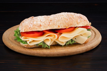 Ciabatta sandwich with lettuce , prosciutto and  cheese on wooden board