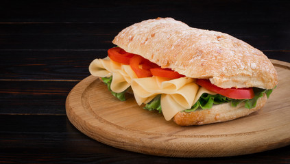 Ciabatta sandwich with lettuce , prosciutto and  cheese on wooden board with copy space