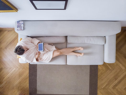 Mature woman in bathrobe sitting on the couch at home using digital tablet