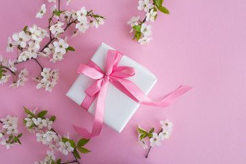 Gift with pink bow and flowering tree branches on the pink background.Top view.Copy space.