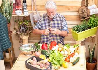 The farmer peels the potatoes. A senior man with white hair works to prepare a healthy vegetable soup for the family. Vintage corner in the garden with plants, herbs and flowers.