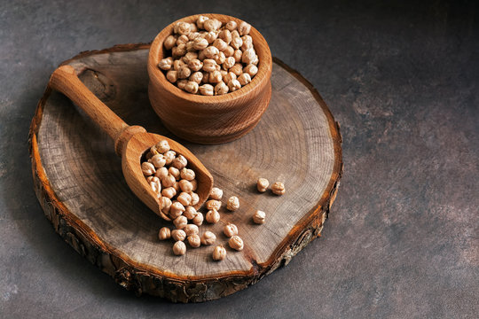 Raw chickpeas wooden scoop and bowl on a stump board, seen from the front. Selective focus,copy space.