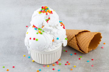 plate of vanilla ice cream scoop swith sprinkles and waffle cones