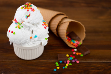 plate of vanilla ice cream scoop swith sprinkles chocolate pieces and waffle cones