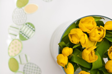 Fototapeta na wymiar Yellow tulips in glass vase as Easter table decoration.