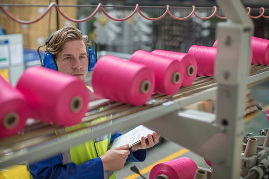 Man wearing ear defenders working at spool machine in factory