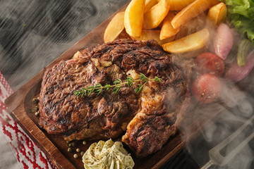 Ribeye steak with potatoes, onions and baked cherry tomatoes. Juicy steak with flavored butter