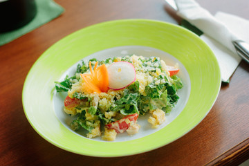 Salad with radish, carrot, lettuce and cheese in a green plate.