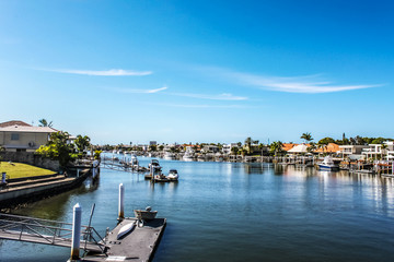 Fototapeta na wymiar Canal in tropical setting with boat docks and moored boats by each waterside house and palm trees under blue sky
