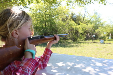 Girl with blond hair doing target practice with a 22 rifle