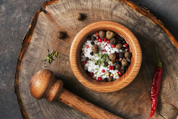 Closeup spices peppercorn, salt, herbs in a wooden mortar on a stump board, overhead view.