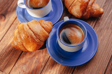 two cups of coffee and croissants on a wooden background, good light, morning atmosphere
