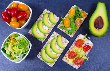 Healthy snack from wholegrain rye crispbread cracker with cherry tomatoes, avocado and salad. Proper nutrition.