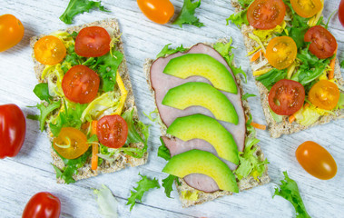 Healthy snack from wholegrain rye crispbread cracker with cherry tomatoes, avocado and salad. Proper nutrition.