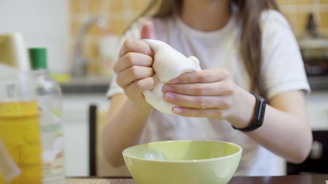 focus on teen girl hands squeezing and stretching white fluffy slime