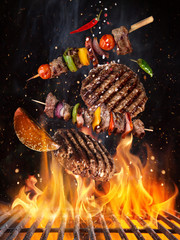 Tasty beef steaks and skewers flying above cast iron grate with fire flames.