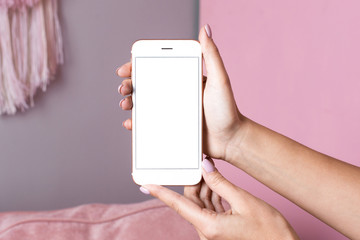 Female hands hold mobile phone with white screen mock up on a pink interior background