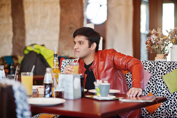 Stylish indian man in casual wear sitting indoor cafe and drink juice.