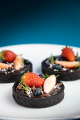 Cookie crust chocolate tart with Blueberry and strawberry set on Blue Background.