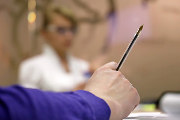 Business meeting in office, male hand with a pen on blurred background of a girl with glasses. Сoncept of discussion, teamwork, presentation, educational course