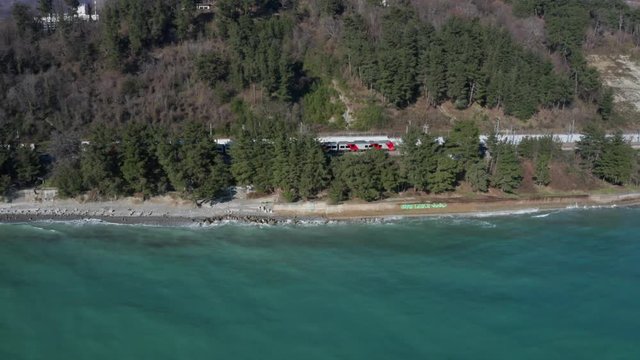 Aerial drone. High-speed train rides along the coast. Journey to the sea. Parallel camera shooting. Railway by the sea. Bird's-eye view. Railage. Train goes to Sochi