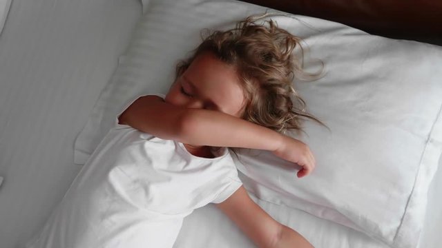 Portrait of little cute girl is waking up, stretching and smiling on the white linen in bed at the morning.