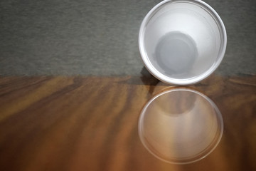 empty  plastic cup standing on wooden table  with reflection and grey background 