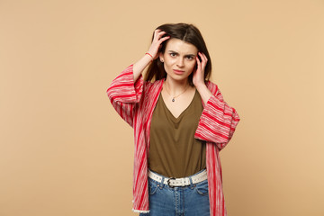 Frustrated displeased young woman in casual clothes looking camera, putting hands on head isolated on pastel beige background in studio. People sincere emotions, lifestyle concept. Mock up copy space.