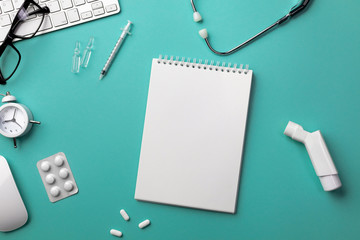 Stethoscope in doctors desk with keyboard, alarm clock, glasses, inhaler, syringe, ampoules, inhaler and pills