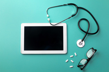 Stethoscope in doctors desk with tablet, glasses and pills