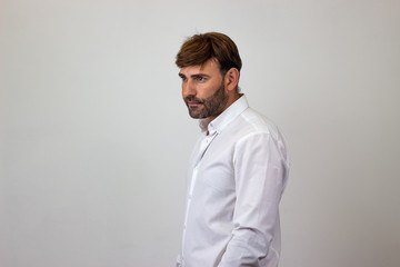 Fashion portrait of handsome young man with brown hair looking ashamed, facing forwards and looking at the horizon. Isolated on white background.