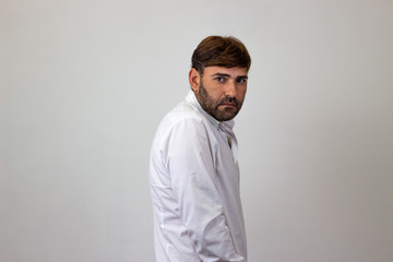 Obraz premium Fashion portrait of handsome young man with brown hair looking ashamed, their back facing the camera and looking at the camera. Isolated on white background.