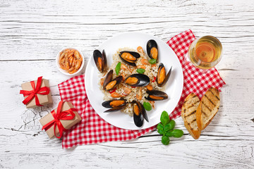 Fried rice with seafood mussels, shrimps and basil in a plate with wineglass, towel,toasted baguette and gift boxes on white cracked wooden table