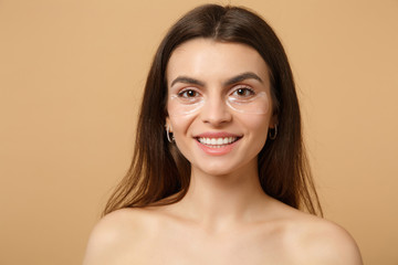 Close up half naked woman 20s with perfect skin, nude make up patches under eyes isolated on beige...