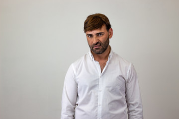 Obraz premium Moda portret przystojny młodzieniec z brązowymi włosami, patrząc udręczony lub zgorzkniały, patrząc w kamerę. Na białym tle