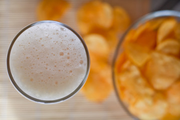 a bowl of potato chips out of focus and a glass of wheat beer top view