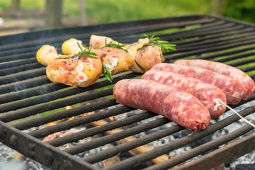 Tasty meat being barbecued on a rustic embers grill in a garden. Chicken with herbs and sausages.