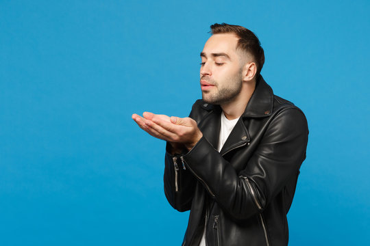 Handsome stylish young bearded man in black leather jacket white t-shirt send air kiss isolated on blue wall background studio portrait. People sincere emotions lifestyle concept. Mock up copy space.