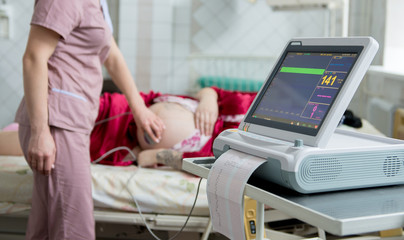 Pregnant woman with electrocardiograph check up for her baby. Fetal heart monitoring. Diagnostic, healthcare, medical service
