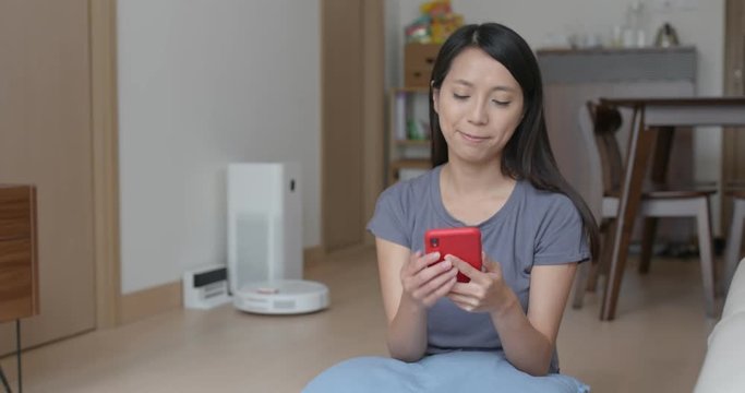 Woman use of mobile phone to control robotic vacuum cleaner at home