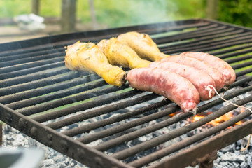 Tasty meat being barbecued on a rustic embers grill in a garden. Chicken with herbs and sausages.
