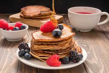 Pouring honey on Pancakes with blueberries and strawberries and cup of red juice