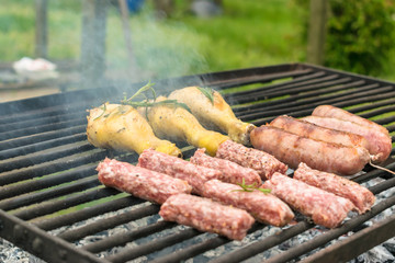 Tasty meat being barbecued on a rustic embers grill in a garden. Chicken with herbs and sausages.