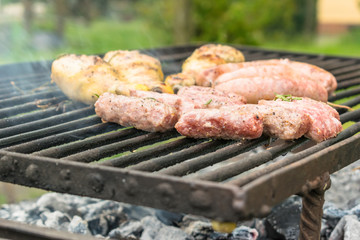 Tasty meat being barbecued on a rustic embers grill in a garden. Chicken with herbs and sausages.