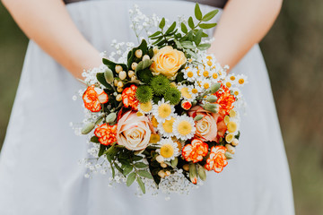 Frau hält sommerlichen, frühlingshaften, gelb, orange Blumenstrauß während einer Hochzeit in ihren Händen