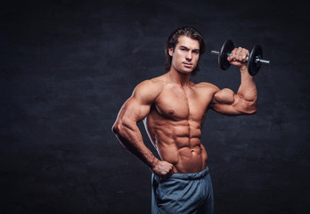 Fototapeta na wymiar Attractive shirtless bodybuilder is doing exercise with dumbbell. There is dark background.