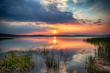 Obraz na płótnie Canvas Beautiful sunset scene on the lake with stunning water reflection of Sun and clouds sky in summer evening - Image