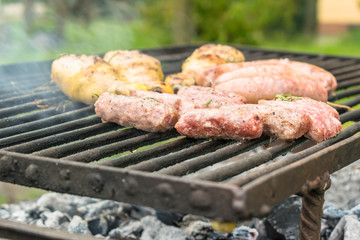Tasty meat being barbecued on a rustic embers grill in a garden. Chicken with herbs and sausages.