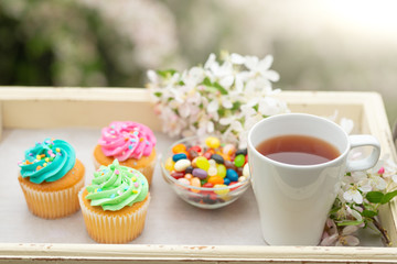 Fototapeta na wymiar Bright cakes. Cupcakes with colored candies and a cup of coffee or tea on a tray with a bright color background, a sunny morning and a bright mood. spring background